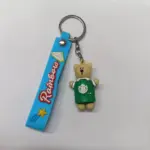 Portachiavi orsetto colorato con cinturino azzurro e maglietta verde su sfondo neutro