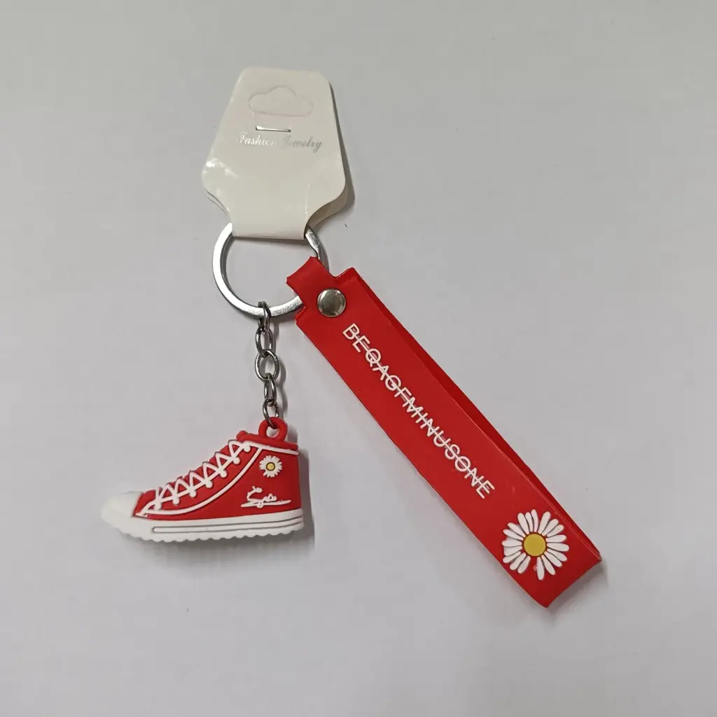 Portachiavi sneaker rossa in gomma con dettagli bianchi e nastro decorativo rosso su sfondo neutro