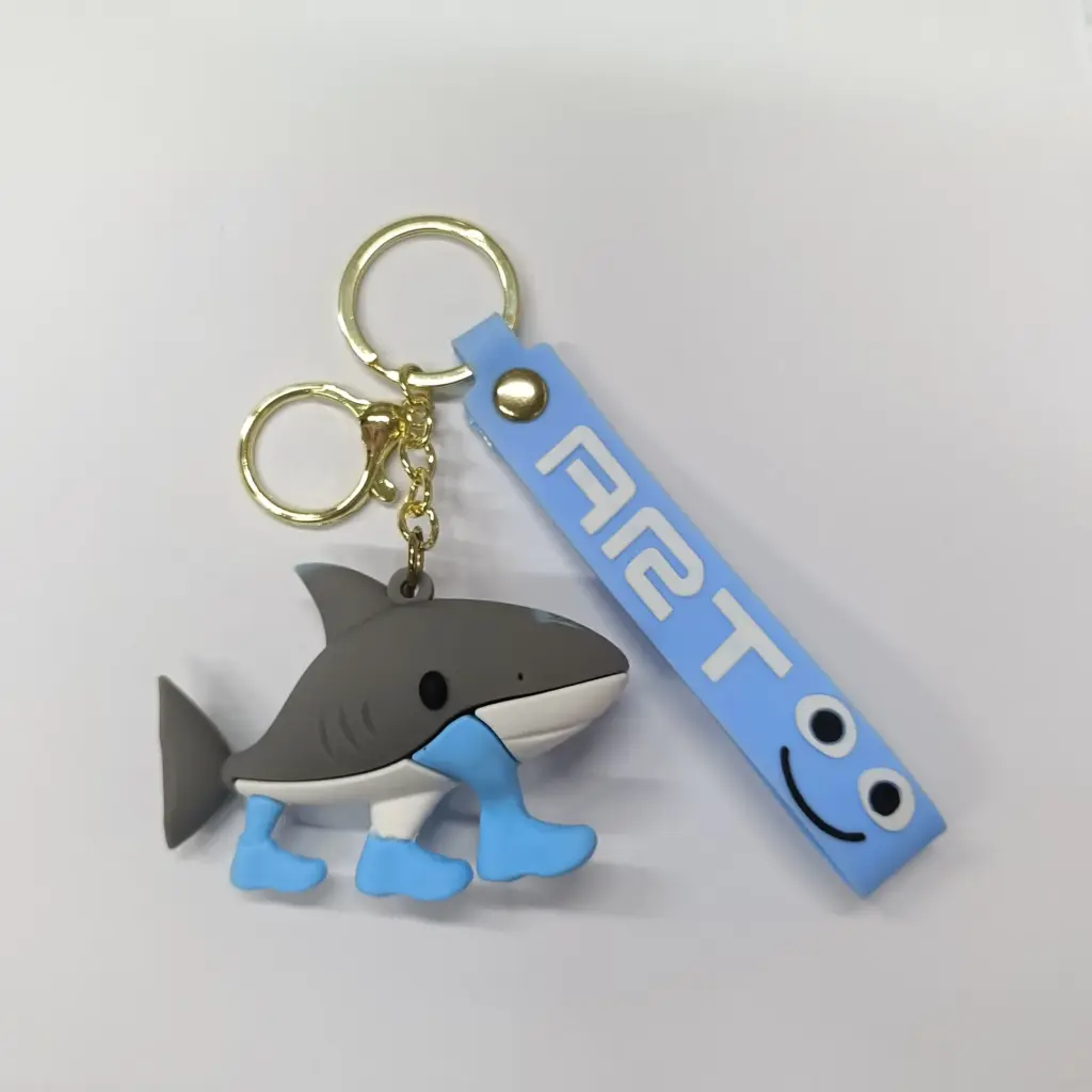 Portachiavi squalo grigio in gomma con pinne azzurre e targhetta azzurra con faccina sorridente