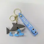 Portachiavi squalo grigio in gomma con pinne azzurre e targhetta azzurra con faccina sorridente