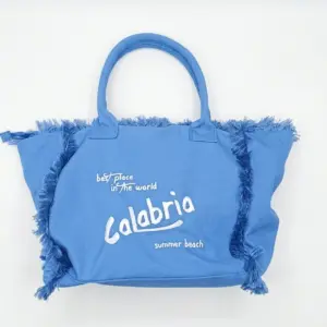 Borsa a mano in tessuto azzurro con frange laterali e scritta bianca Calabria, best place in the world, summer beach
