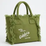 Borsa tote a mano in canvas verde oliva con frange laterali e scritta Calabria ricamata in bianco, manici rigidi e struttura rettangolare