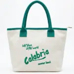 Borsa tote bianca con manici verde smeraldo e scritta Calabria best place in the world summer beach in corsivo verde sul fronte, chiusura a zip