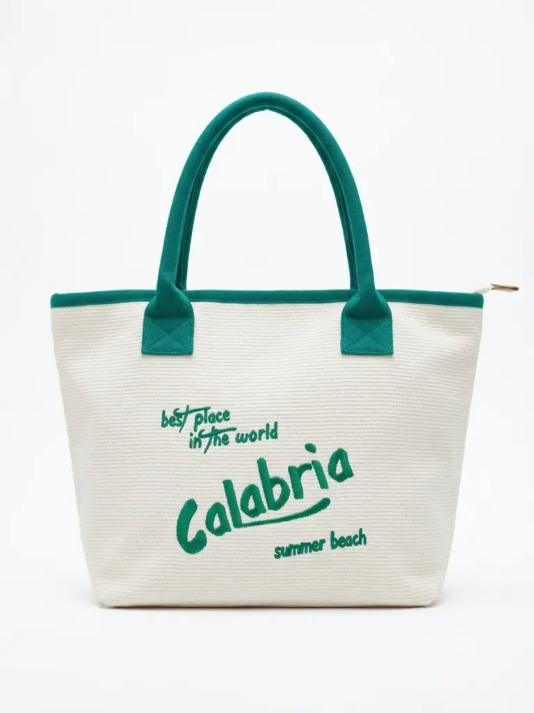 Borsa tote bianca con manici verde smeraldo e scritta Calabria best place in the world summer beach in corsivo verde sul fronte, chiusura a zip