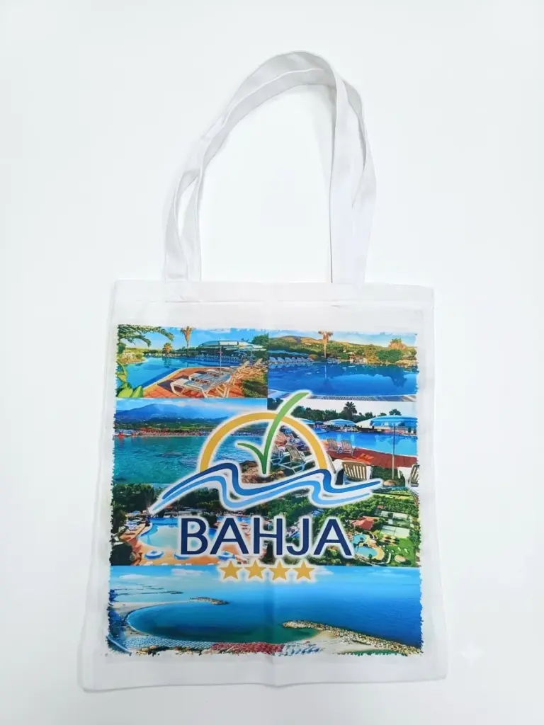 Borsa tote bianca in tela con manici lunghi bianchi e collage fotografico multicolore del Villaggio Bahja con logo a quattro stelle dorate sul fronte
