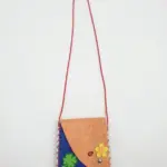 Borsetta a tracolla in tessuto beige e blu cobalto con cuciture rosse, quadrifoglio verde e fiore giallo applicati, cordino rosso