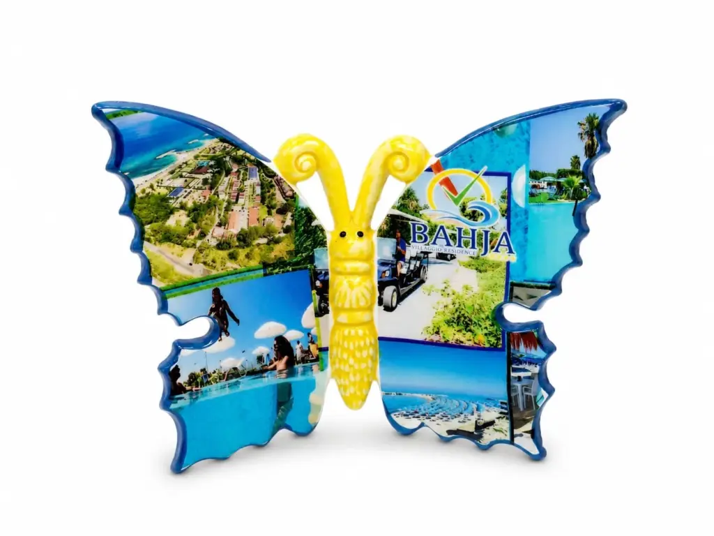Farfalla da appoggio in resina blu con collage di vedute del Bahja Villaggio Residence; corpo centrale giallo tridimensionale con antenne arricciate.