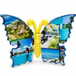 Farfalla da appoggio in resina blu con collage di vedute del Bahja Villaggio Residence; corpo centrale giallo tridimensionale con antenne arricciate.