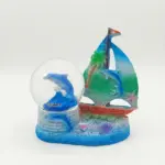 Palla di neve con delfino blu e scritta Calabria, affiancata da scultura in resina con barca a vela blu-verde su base azzurra.