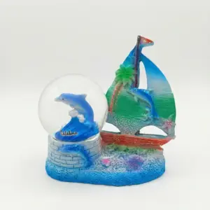 Palla di neve con delfino blu e scritta Calabria, affiancata da scultura in resina con barca a vela blu-verde su base azzurra.