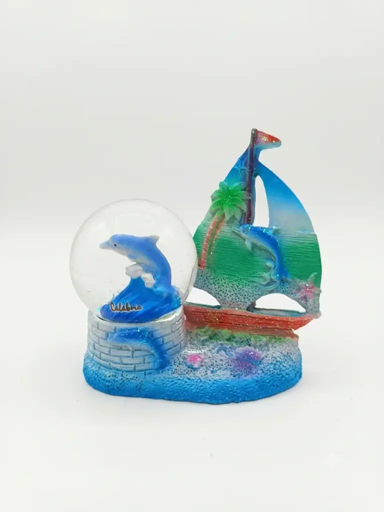 Palla di neve con delfino blu e scritta Calabria, affiancata da scultura in resina con barca a vela blu-verde su base azzurra.