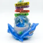 Palla di neve Calabria con delfini blu, sfera con delfino azzurro e glitter, cartelli colorati Buffet Car Big Beach Fish Market Cure Club e gabbiano