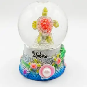 Bolla di vetro con tartaruga marina in resina, guscio rosato glitterato e pinne giallo-verdi, base decorata con perla e scritta Calabria