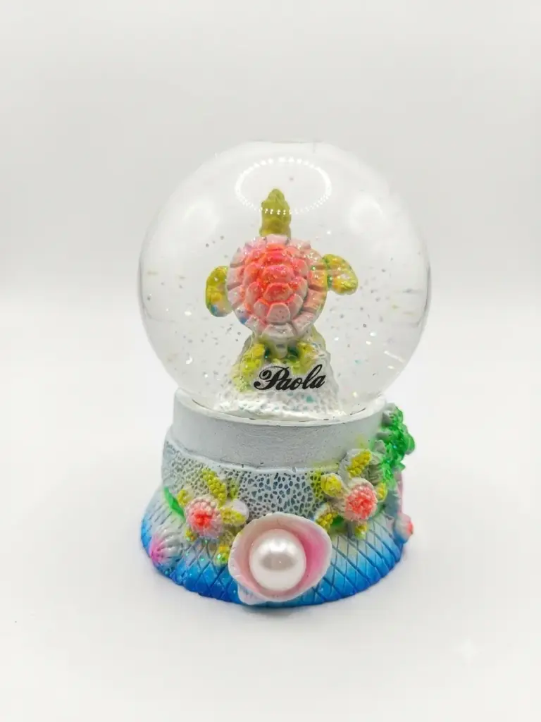 Bolla di neve con tartaruga marina rosa-corallo, base azzurra con fiori in rilievo e conchiglia con perla, scritta Paola