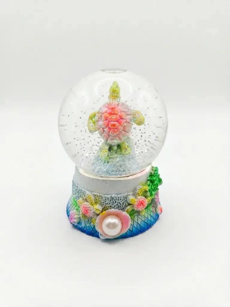 Palla di neve con tartaruga marina carapace rosa corallo e pinne verde lime, base decorata con conchiglie, alghe e perla bianca