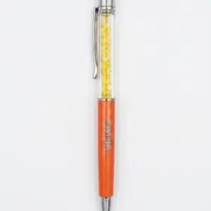 Penna a sfera arancione metallizzato con sezione trasparente e cristalli gialli, gommino arancione, clip cromata, scritta BAHJA incisa sul corpo