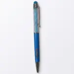 Penna a sfera con fusto trasparente riempito di cristalli azzurri, impugnatura blu con scritta Bahja incisa e puntale stilo azzurro in cima