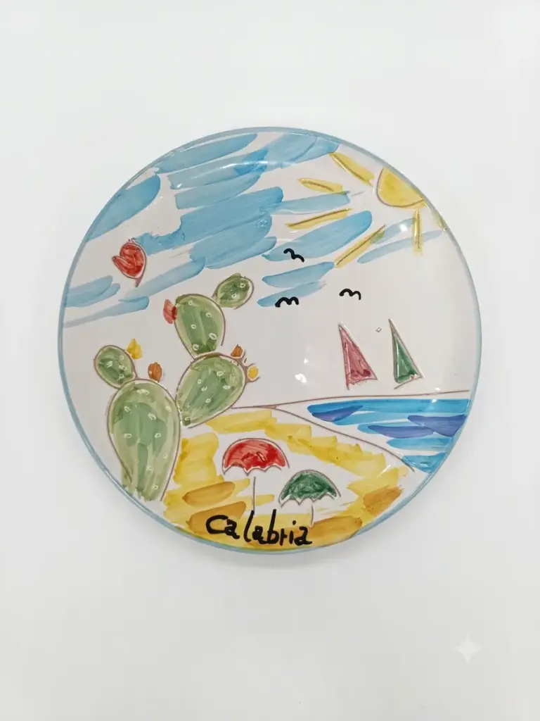 Piatto ceramica tondo con fichi d'india verdi, mare azzurro, barche a vela rosse e verdi, ombrelloni, sole e scritta Calabria