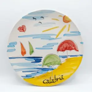 Piatto ceramica Calabria con mare azzurro, barche a vela arancio e verde, ombrelloni rosso e verde sulla spiaggia gialla, sole e gabbiani neri.
