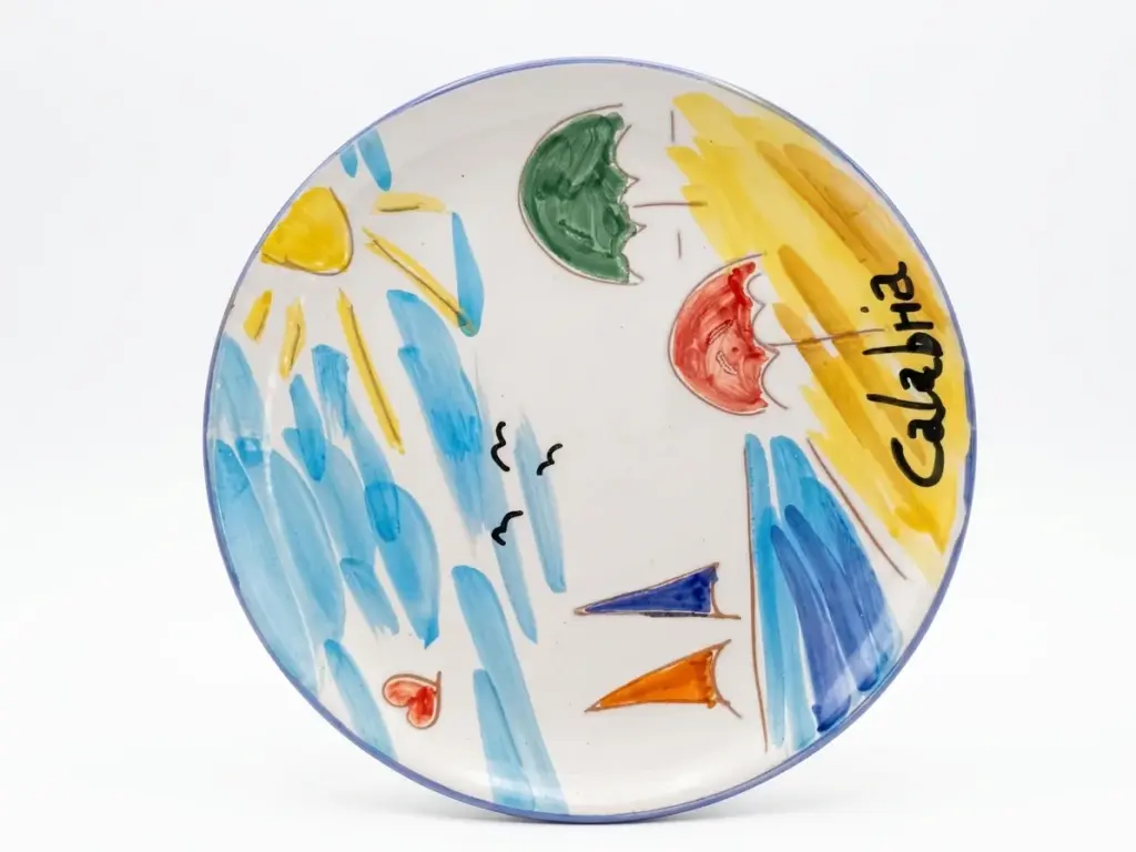 Piatto in ceramica bordo azzurro con scritta Calabria in nero, sole giallo, onde azzurre, ombrelloni verde e rosso, barche a vela blu e arancione
