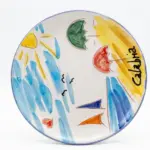 Piatto in ceramica bordo azzurro con scritta Calabria in nero, sole giallo, onde azzurre, ombrelloni verde e rosso, barche a vela blu e arancione