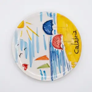 Piatto ceramica rotondo con sole giallo e scritta Calabria, ombrelloni blu e rosso, barche arancioni e verdi, pennellate azzurre di mare