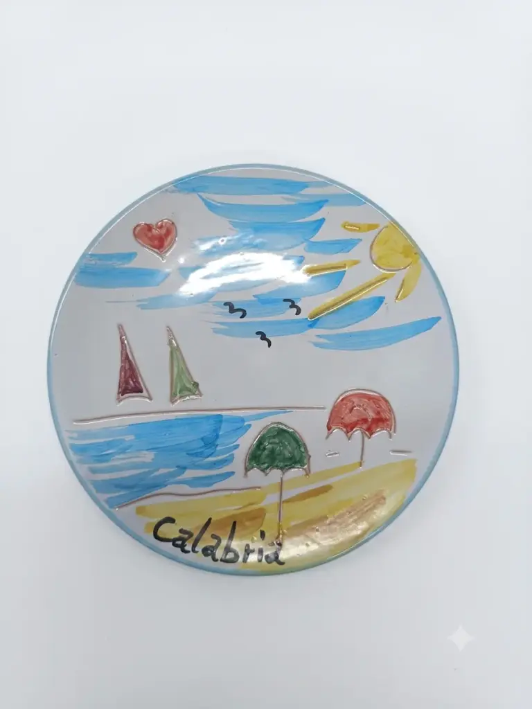 Piatto ceramica rotondo con scena balneare: mare azzurro, barche a vela rossa e verde, ombrelloni, sole e scritta Calabria in nero