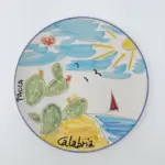 Piatto in ceramica con bordo blu, fichidindia verdi, mare azzurro, barca a vela rossa, gabbiani e scritte Paola e Calabria
