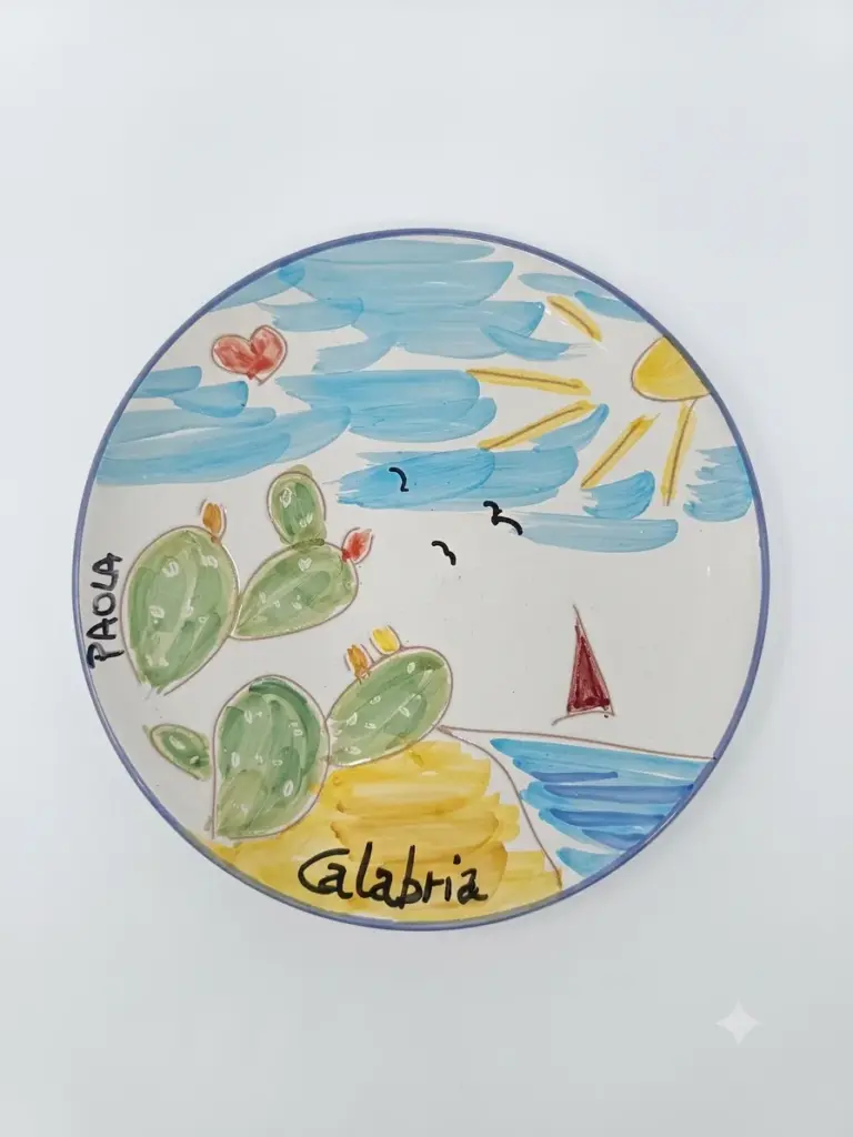 Piatto in ceramica con bordo blu, fichidindia verdi, mare azzurro, barca a vela rossa, gabbiani e scritte Paola e Calabria