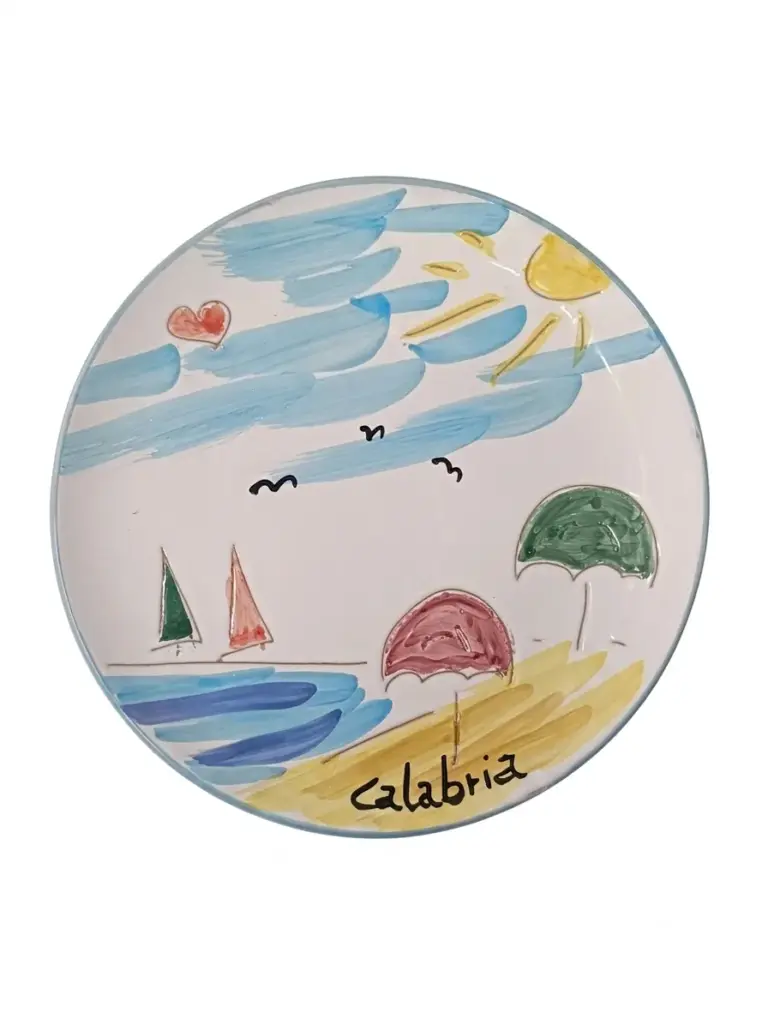 Piatto circolare in ceramica: scena balneare con barche a vela, ombrelloni rosa e verde, sole, gabbiani e scritta Calabria sulla sabbia