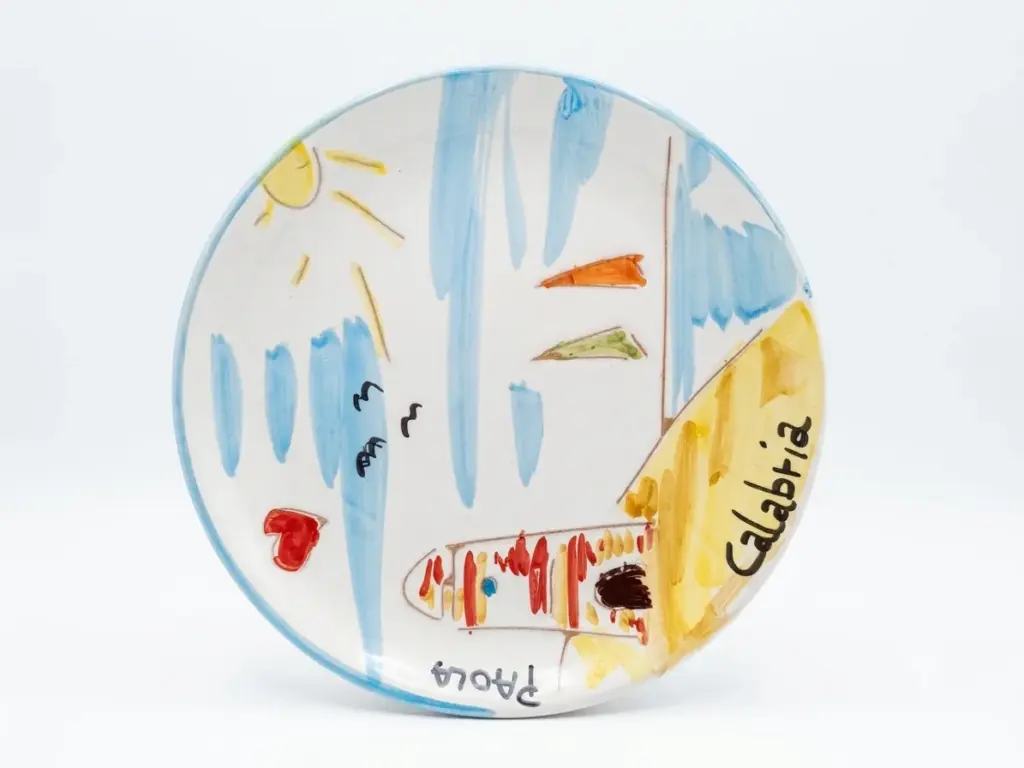 Piatto ceramica con scena marina pitturata: barche multicolori, sole giallo, gabbiani neri, cuore rosso, scritta Calabria e Paola, bordo azzurro