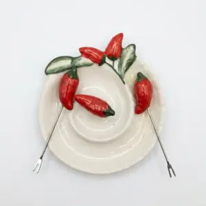 Piatto ceramica bianca a spirale con peperoncini rossi in rilievo, foglie verdi e due forchettine metalliche per aperitivo