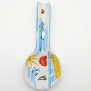 Poggiamestolo in ceramica bianca con pennellate azzurre, sole giallo, cuore rosso e scritta Calabria sul manico