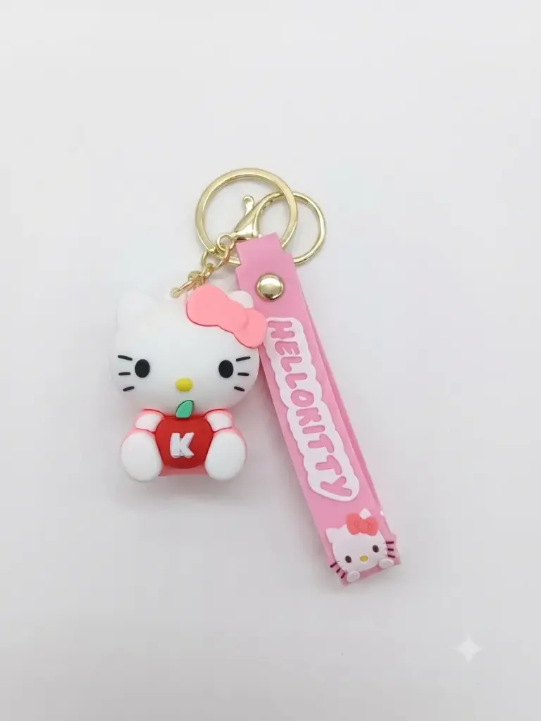 Portachiavi Hello Kitty: ciondolo bianco con fiocco rosa e mela rossa lettera K, cinturino in gomma rosa con scritta HELLO KITTY e moschettone dorato.