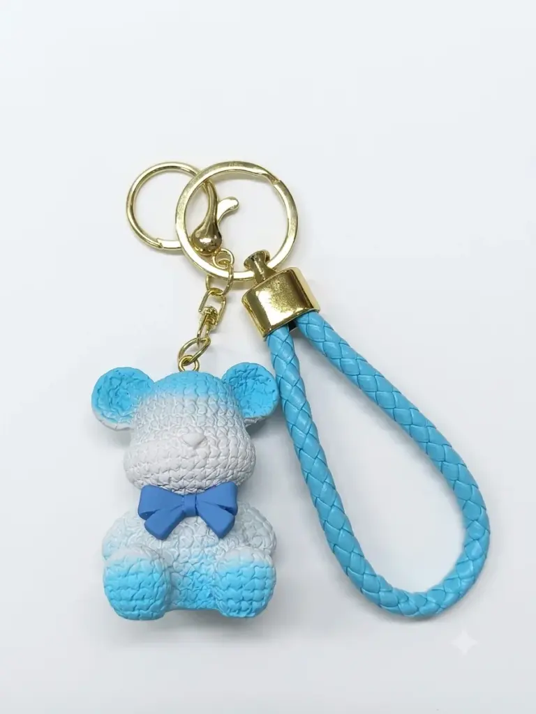 Portachiavi con orsetto in resina azzurra e bianca, texture a rilievo e fiocchetto blu cobalto, cordoncino intrecciato azzurro con hardware dorato