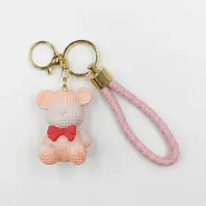 Portachiavi orsetto tridimensionale rosa-pesca e bianco con texture a maglia, fiocco rosso al collo, cordino intrecciato rosa e anelli dorati