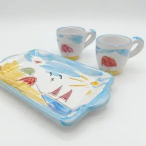 Set tre pezzi ceramica bianca: vassoio rettangolare e due tazzine con bordi azzurri, decori naif ombrelloni colorati, velieri rossi e sole