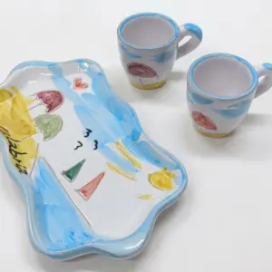 Set tazzine caffè ceramica bianca con vassoio sagomato ondulato, decori azzurri, ombrelloni colorati e scritta Calabria in nero