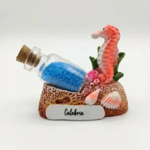 Composizione decorativa Calabria con cavalluccio marino in resina corallo, bottiglietta di vetro con sabbia blu, conchiglie e base a scoglio ocra