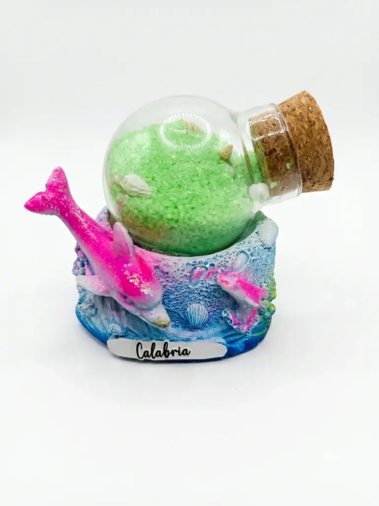 Bolla di vetro con sabbia verde brillante e tappo in sughero su base resina azzurra con delfino rosa glitterato e scritta Calabria