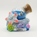 Bolla di vetro con sabbia blu e conchiglie su base in resina con stella marina bianca glitterata, pesciolini viola e rosa, scritta Calabria