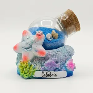 Bolla di vetro con sabbia blu e conchiglie su base in resina con stella marina bianca glitterata, pesciolini viola e rosa, scritta Calabria