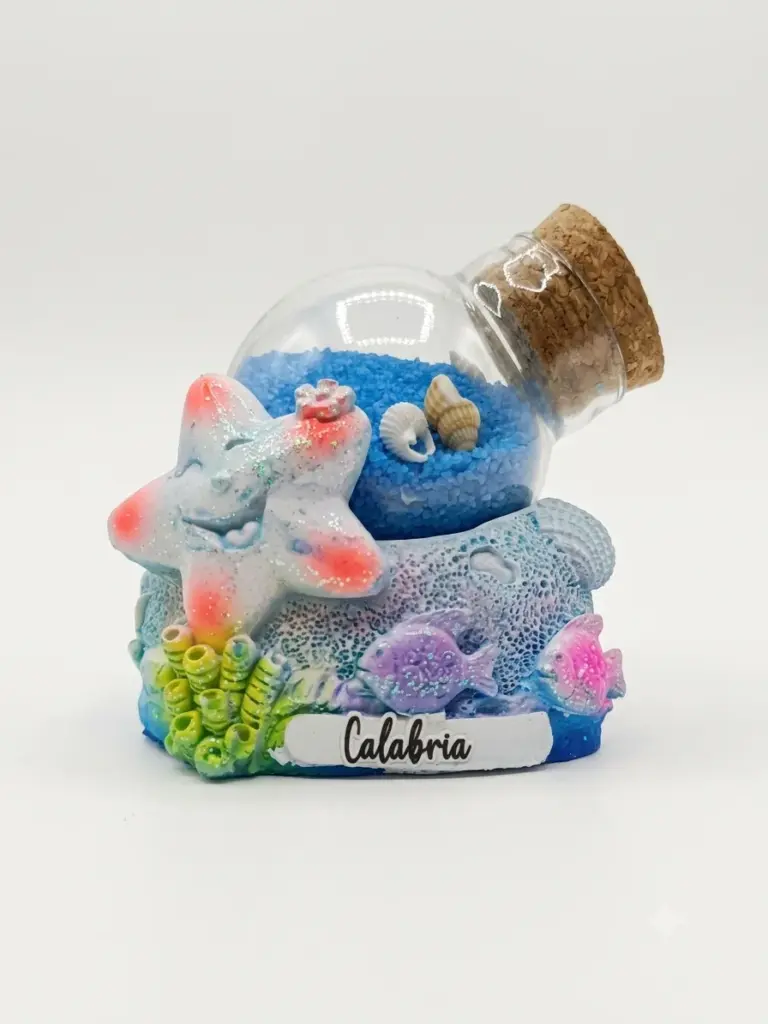 Bolla di vetro con sabbia blu e conchiglie su base in resina con stella marina bianca glitterata, pesciolini viola e rosa, scritta Calabria