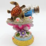 Soprammobile in resina con tartaruga marina arancione, coralli rosa-fucsia, fiore viola e bottiglia di vetro con sabbia blu e scritta Calabria