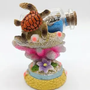 Soprammobile in resina con tartaruga marina arancione, coralli rosa-fucsia, fiore viola e bottiglia di vetro con sabbia blu e scritta Calabria