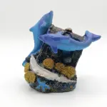 Soprammobile in resina con due delfini blu e viola su relitto scuro, base glitterata dorata, stella marina azzurra e conchiglia argentata