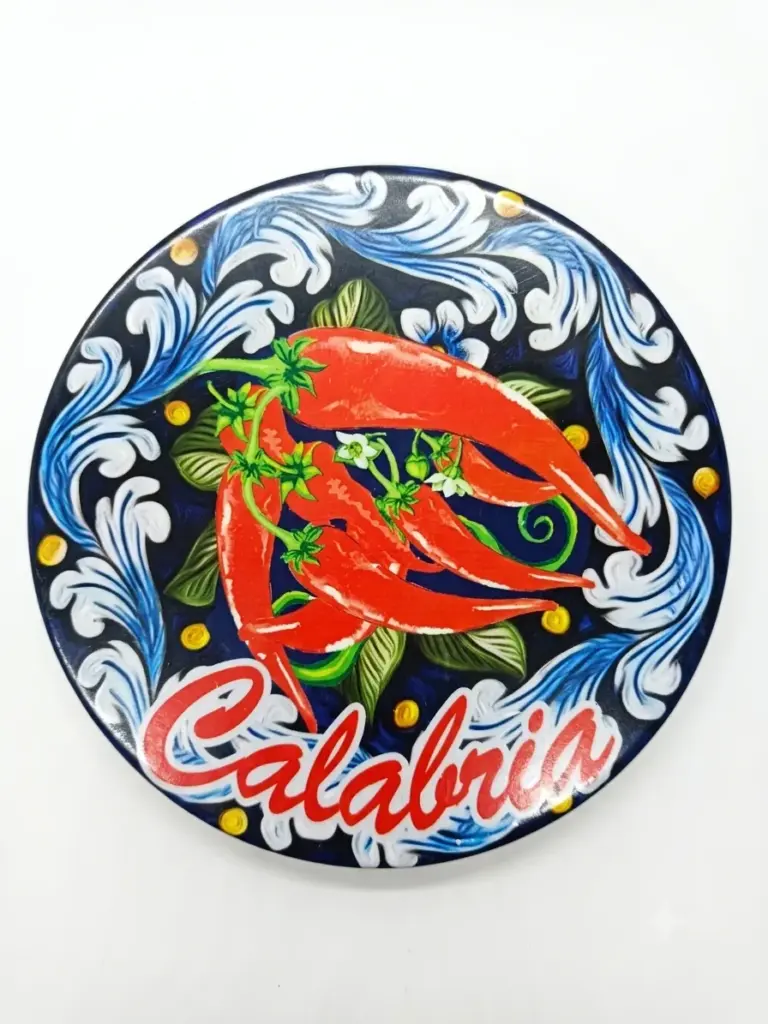 Sottopentola rotondo ceramica, tre peperoncini rossi su fondo blu scuro con volute bianche e scritta Calabria in corsivo rosso