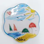 Sottopentola ceramica forma ondulata, scena marina con barca a vela, ombrelloni, sole e scritta Calabria