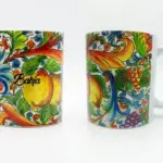 Tazza ceramica bianca: fronte con limoni gialli, arabeschi rosso-arancio e scritta corsiva Bahja; retro con grappoli d'uva viola e volute blu.
