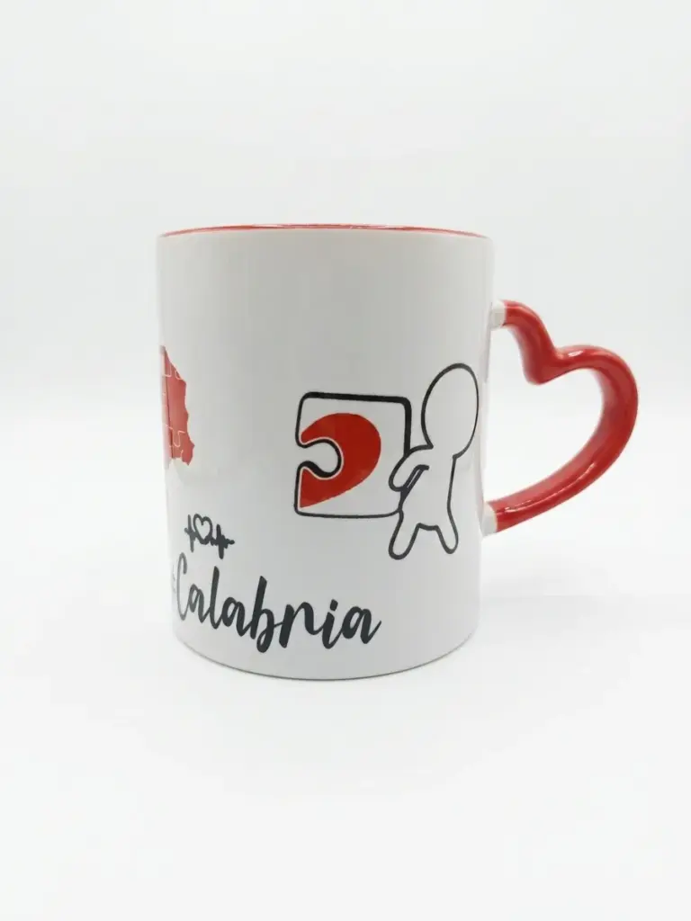 Tazza ceramica bianca con manico rosso a forma di cuore, sagoma rossa della Calabria, grafica puzzle stilizzata e scritta Calabria in corsivo nero